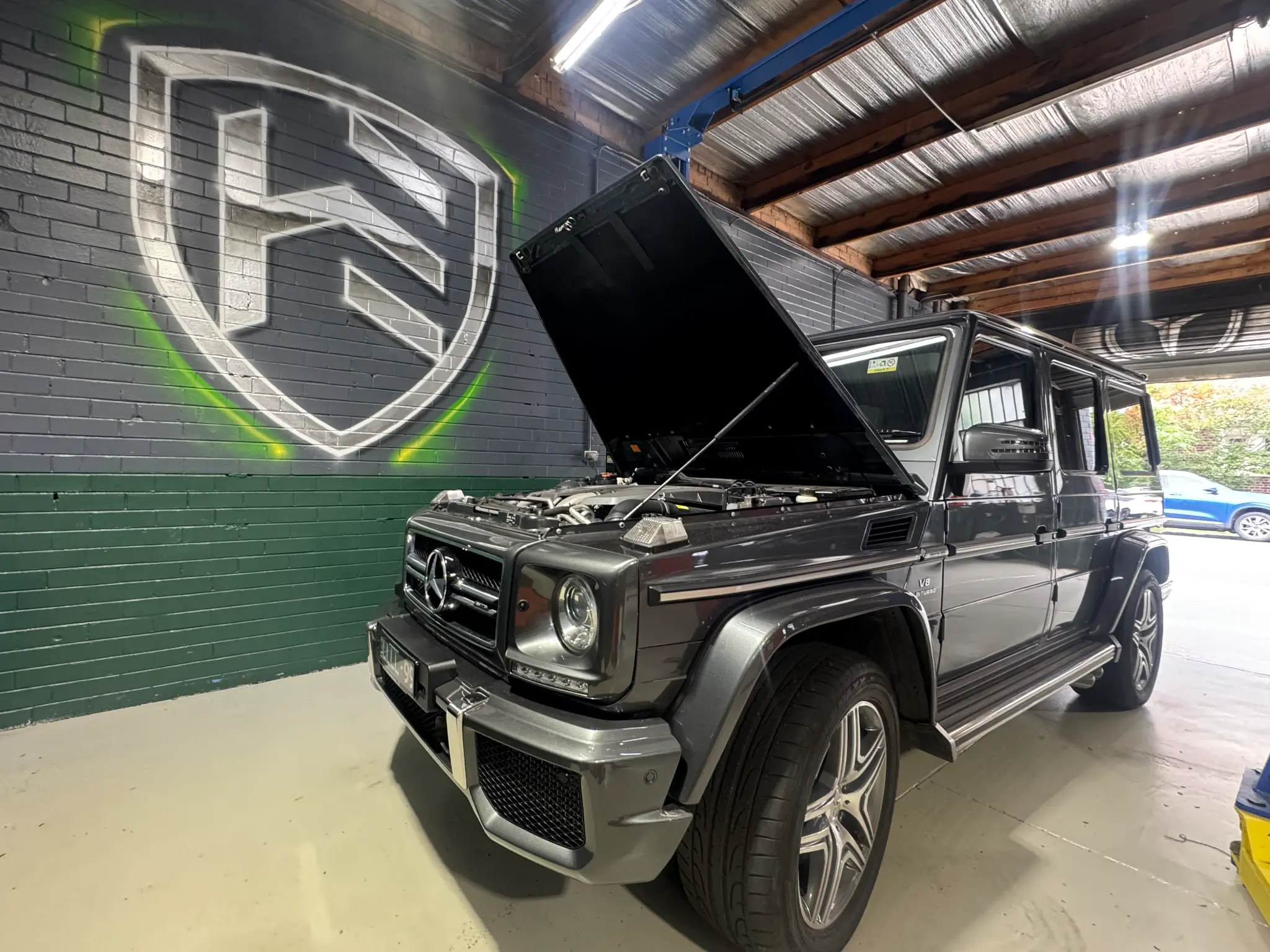 Mercedes-AMG G63 with hood open showing V8 biturbo engine, Hawthorn Eurotech shield logo on wall