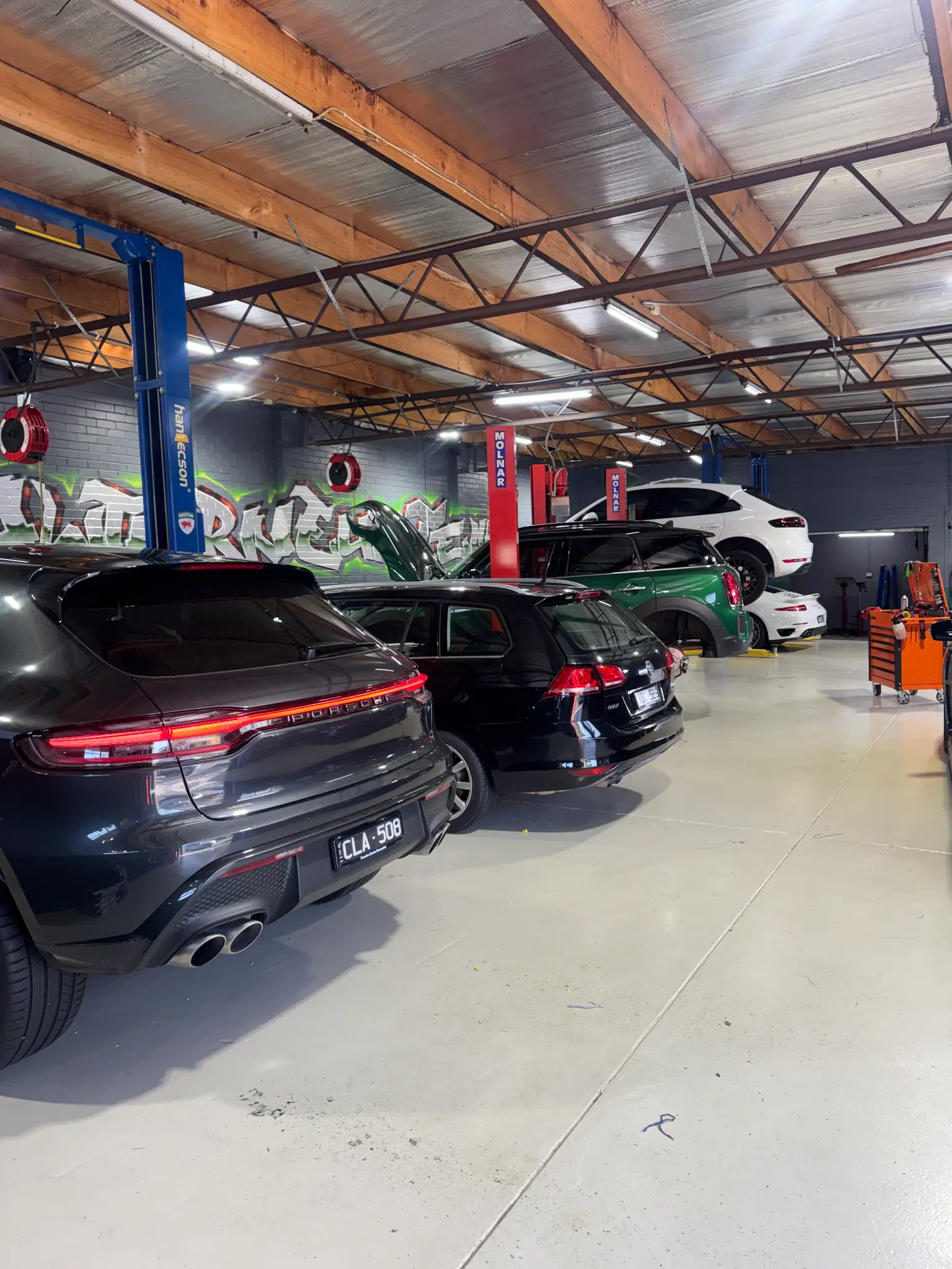 Porsche Cayenne, VW Golf R, green MINI and white Porsche 911 in workshop